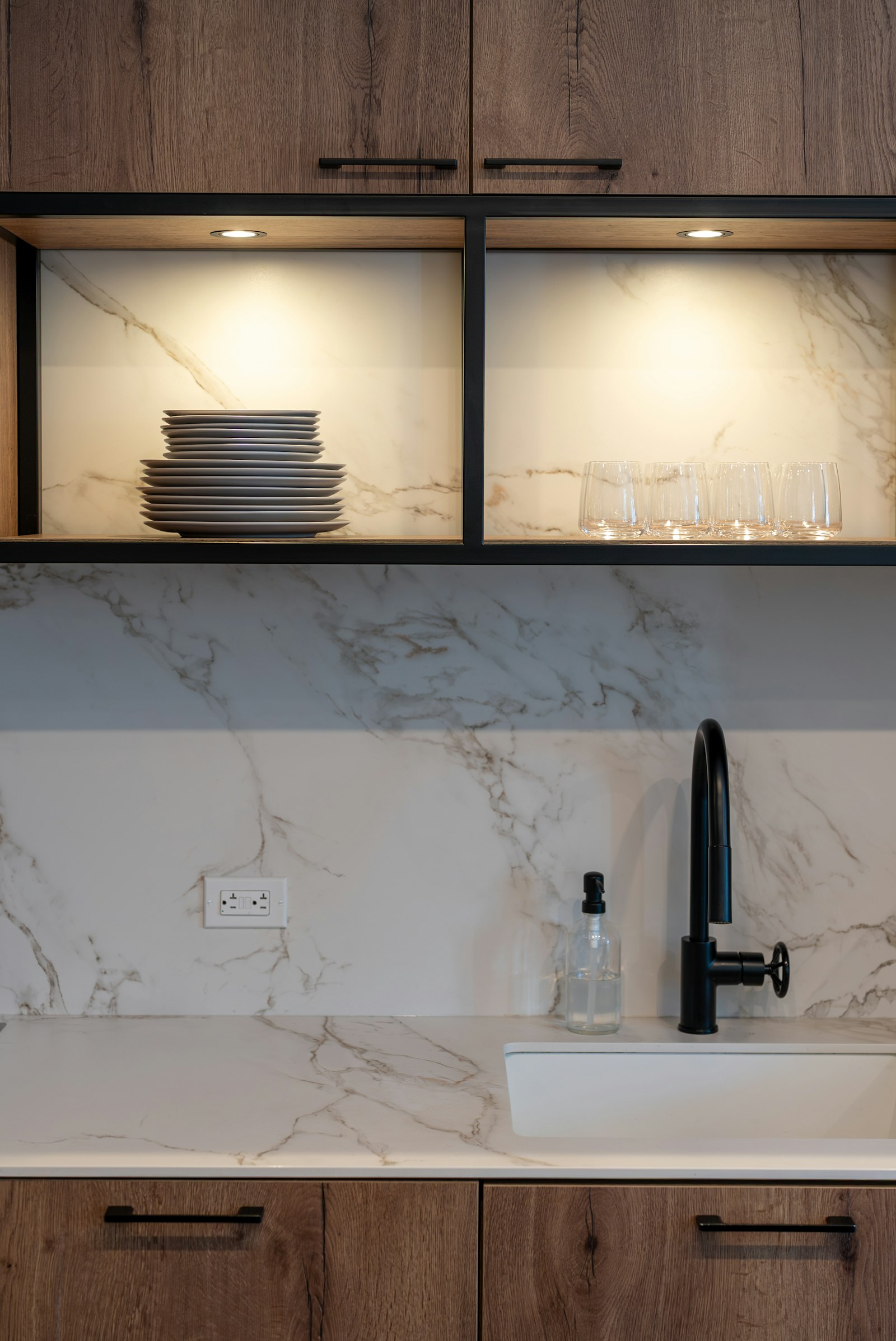 A modern kitchen sink set beneath illuminated cabinets